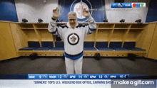a man in a hockey uniform stands in a locker room with his arms in the air