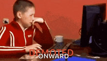 a boy in a red jacket is sitting at a desk in front of a computer screen .