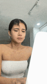 a woman in a white strapless top looks at a laptop