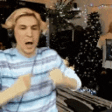 a man wearing headphones is dancing in front of a christmas tree in a living room .