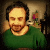 a man wearing headphones and a green shirt is looking down with his eyes closed