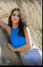 a woman in a blue crop top leaning against a rock