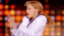 a woman in a white jacket and tie is dancing on a stage in front of a crowd .
