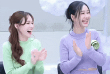 a woman in a green sweater and a woman in a purple sweater are clapping their hands