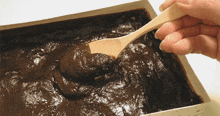 a person holding a wooden spoon over a box of chocolate