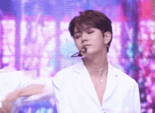 a young man wearing a white jacket and a necklace is standing in front of a purple screen .