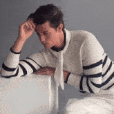 a man wearing a striped sweater leans on a white box