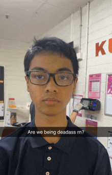 a young man wearing glasses stands in front of a wall that says kc