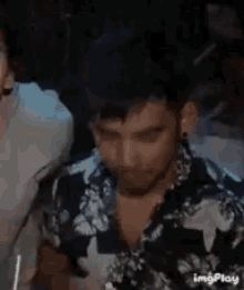 a man in a floral shirt is drinking water from a glass .