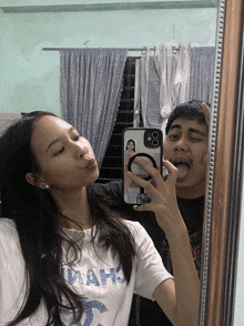 a man and a woman are taking a selfie in front of a mirror and the woman is wearing a shirt that says mah