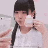 a girl is taking a picture of herself with her phone and holding a cup with whipped cream in it .