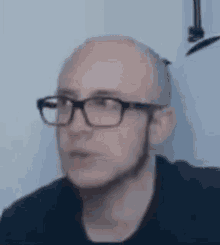 a bald man wearing glasses and a beard is looking at the camera .