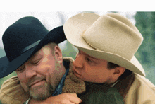 a man in a cowboy hat is hugging another man in a black hat