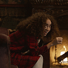 a woman with curly hair is sitting in front of a fireplace smiling