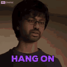 a man wearing glasses and a blue shirt is standing in front of a sign that says hang on .