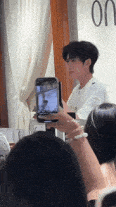 a man in a white shirt is taking a picture of a woman with a cell phone .