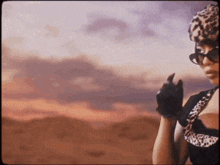 a woman wearing sunglasses and a leopard print hat is standing in a desert .
