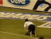 a man is kneeling on a soccer field in front of a ford ad
