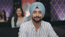 a man wearing a turban and a striped shirt smiles
