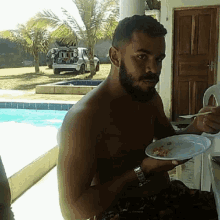 a shirtless man with a beard is eating from a plate