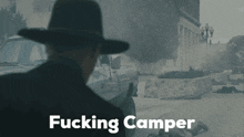 a man in a hat is standing in front of a building with the words " fucking camper " below him
