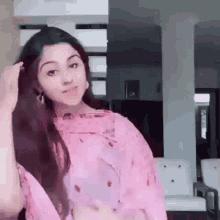 a woman in a pink dress is standing in a living room and holding her hair .