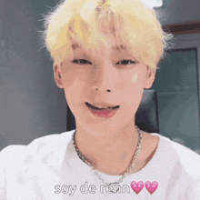 a young man with blonde hair is wearing a white shirt and a necklace and says soy de renn