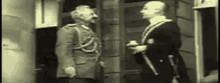 two men in military uniforms are standing next to each other talking .