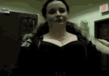 a woman in a black bra is standing in a room with an exit sign on the wall .