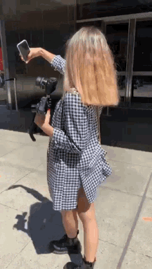 a woman in a plaid shirt is holding a camera and taking a picture with her phone