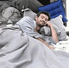 a man is laying in a bed with a gray blanket