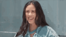 a woman in a denim jacket is laughing with her eyes closed and her mouth open .