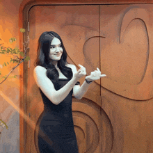 a woman in a black dress stands in front of a wooden door with a swirl design