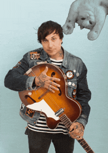 a man in a denim jacket is holding a guitar in front of a cat
