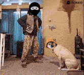 a man in a ninja mask stands next to a dog with a hood on