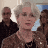 a woman with gray hair is wearing a necklace and earrings and looking at the camera .