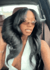 a woman wearing sunglasses and a white top is sitting in the back seat of a car