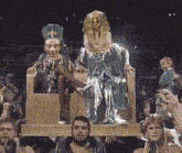 a group of people are sitting in front of a statue of a king and queen
