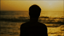 a silhouette of a man standing in front of the ocean at sunset
