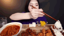 a woman is eating food with chopsticks while sitting at a table .