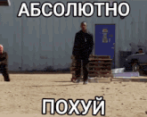 a man in a black suit stands in a dirt field with a blue door behind him