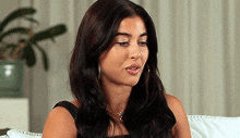 a woman is sitting on a couch with her eyes closed and a plant in the background .