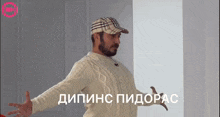 a man with a beard wearing a hat and a sweater with russian writing behind him