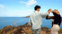 a man and woman are standing on a hill overlooking the ocean