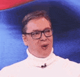 a man wearing glasses and a white turtleneck is talking .