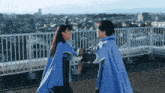 two people wearing blue capes are standing on a balcony