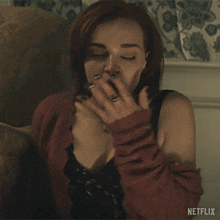 a woman is covering her mouth with her hand and a netflix logo is visible in the corner