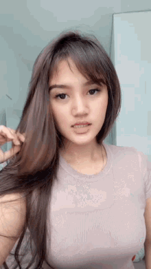a woman with long brown hair is looking at the camera while holding her hair .