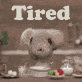 a teddy bear is sitting at a table with the word tired above him