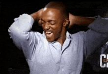 a man in a blue shirt is holding his hands behind his head and smiling .